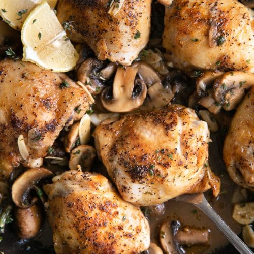 Overhead image of cooked chicken thighs in a light mushroom garlic sauce in a large skillet.