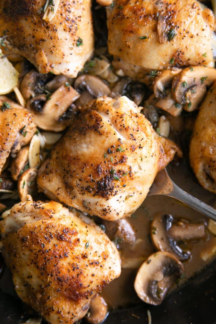 Close up image of juicy bone-in skin-on chicken thighs served with mushrooms.