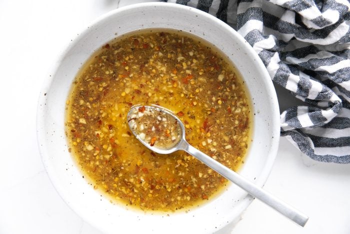 Small white bowl filled with melted butter, minced garlic, red chili flakes, Italian seasoning, Honey, salt, and pepper.