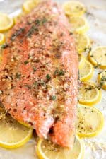Close up image of baked salmon covered in a lemon butter sauce and garnished with fresh thyme.
