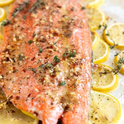 Close up image of baked salmon covered in a lemon butter sauce and garnished with fresh thyme.