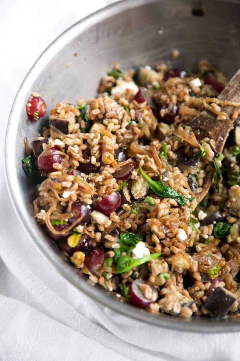 Image of a large mixing bowl filled with a farro salad made up of sliced grapes, spinach, feta cheese, pistachios, caramelized onions, and roasted eggplant.