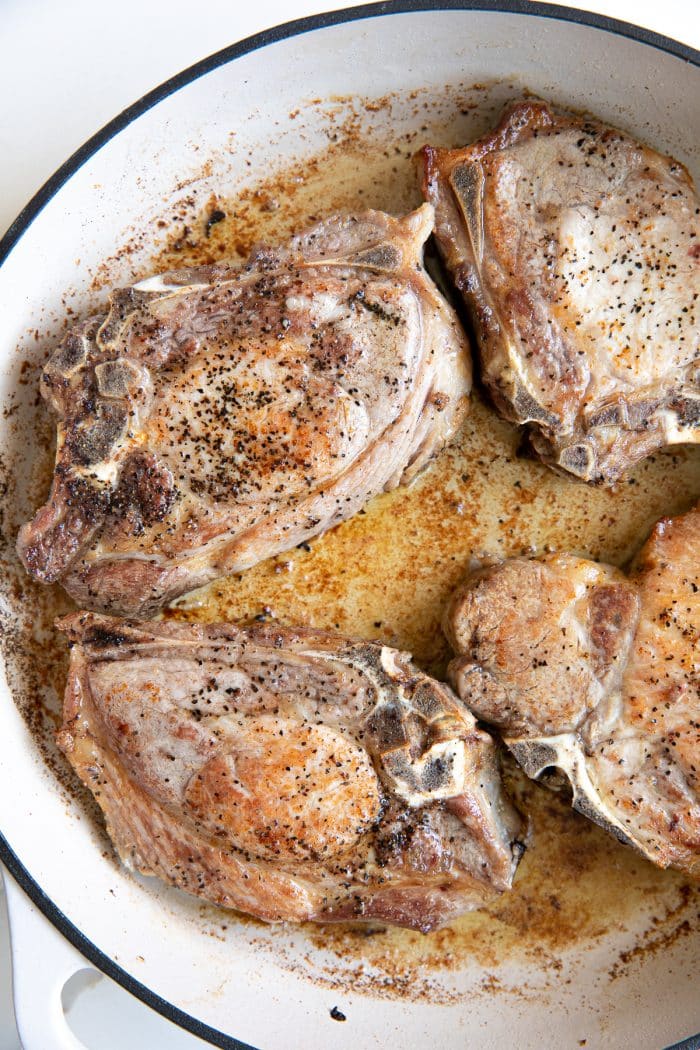 Pork chops searing in a hot skillet with melted butter and olive oil.