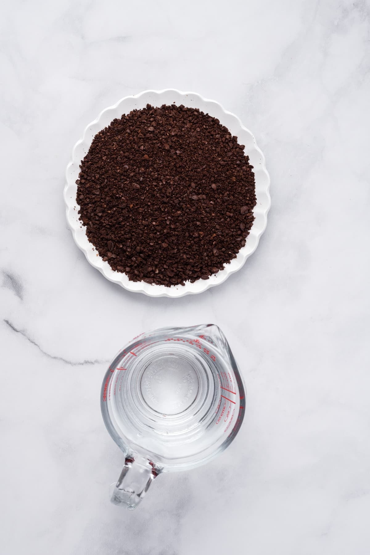 Overhead image of coffee grounds and a measuring cup filled with water.