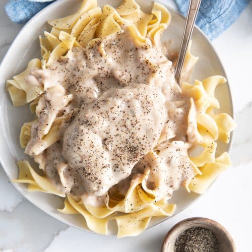 Overhead image of a plate filled with egg noodles and topped with a large pork chop with mushroom gravy.