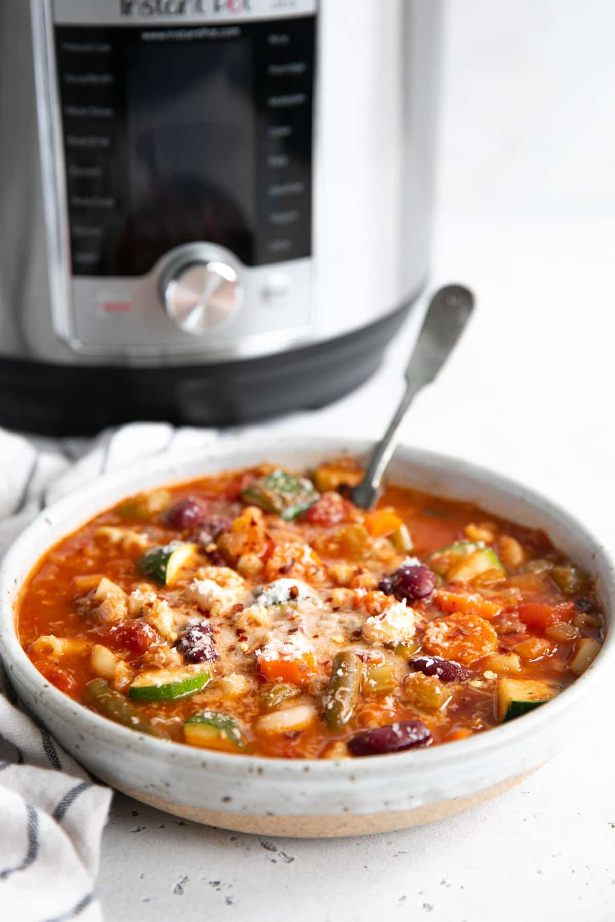 Image of a bowl filled with minestrone soup garnished with grated parmesan cheese.