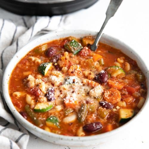 Image of a round shallow bowl filled with minestrone soup garnished with grated parmesan cheese.