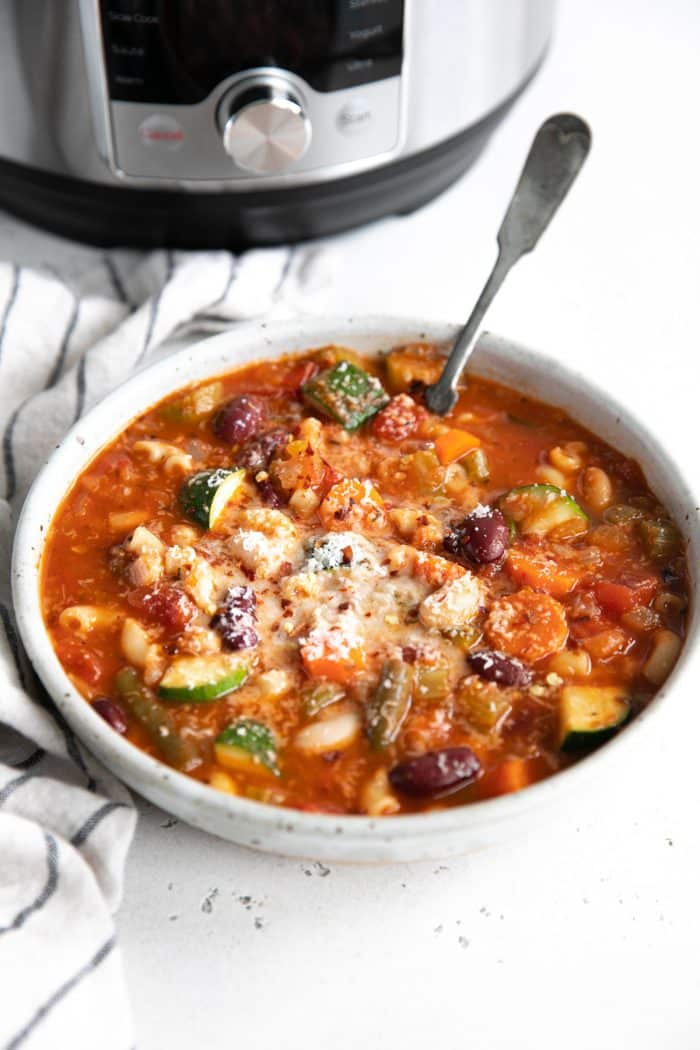 Image of a round shallow bowl filled with minestrone soup garnished with grated parmesan cheese.