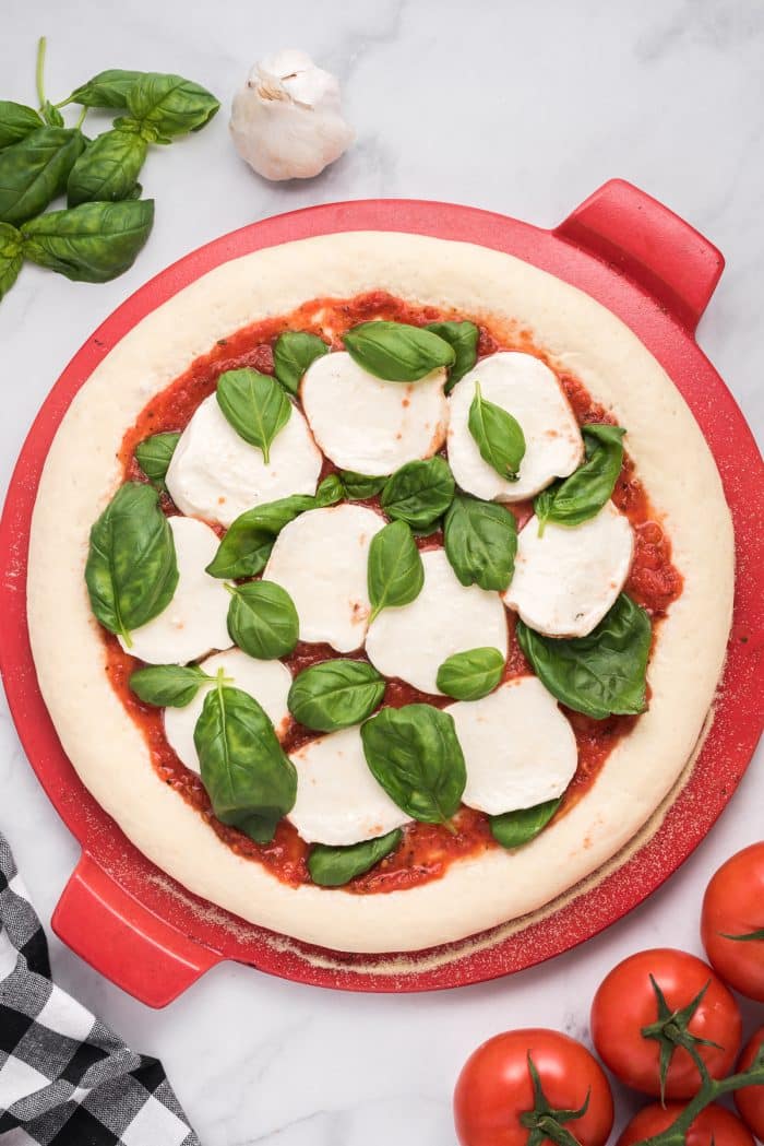 Overhead image of rolled out pizza dough covered with pizza sauce, mozzarella, and fresh basil.