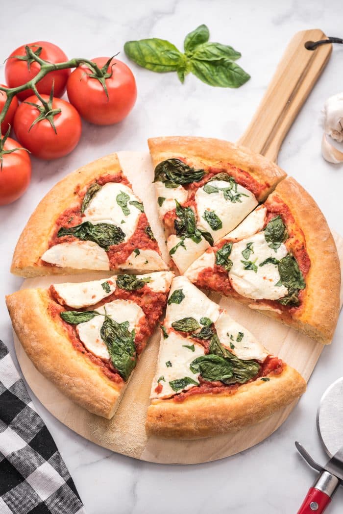 Image of a baked pizza with pizza sauce, fresh mozzarella, and fresh basil, sliced into 5 pieces.