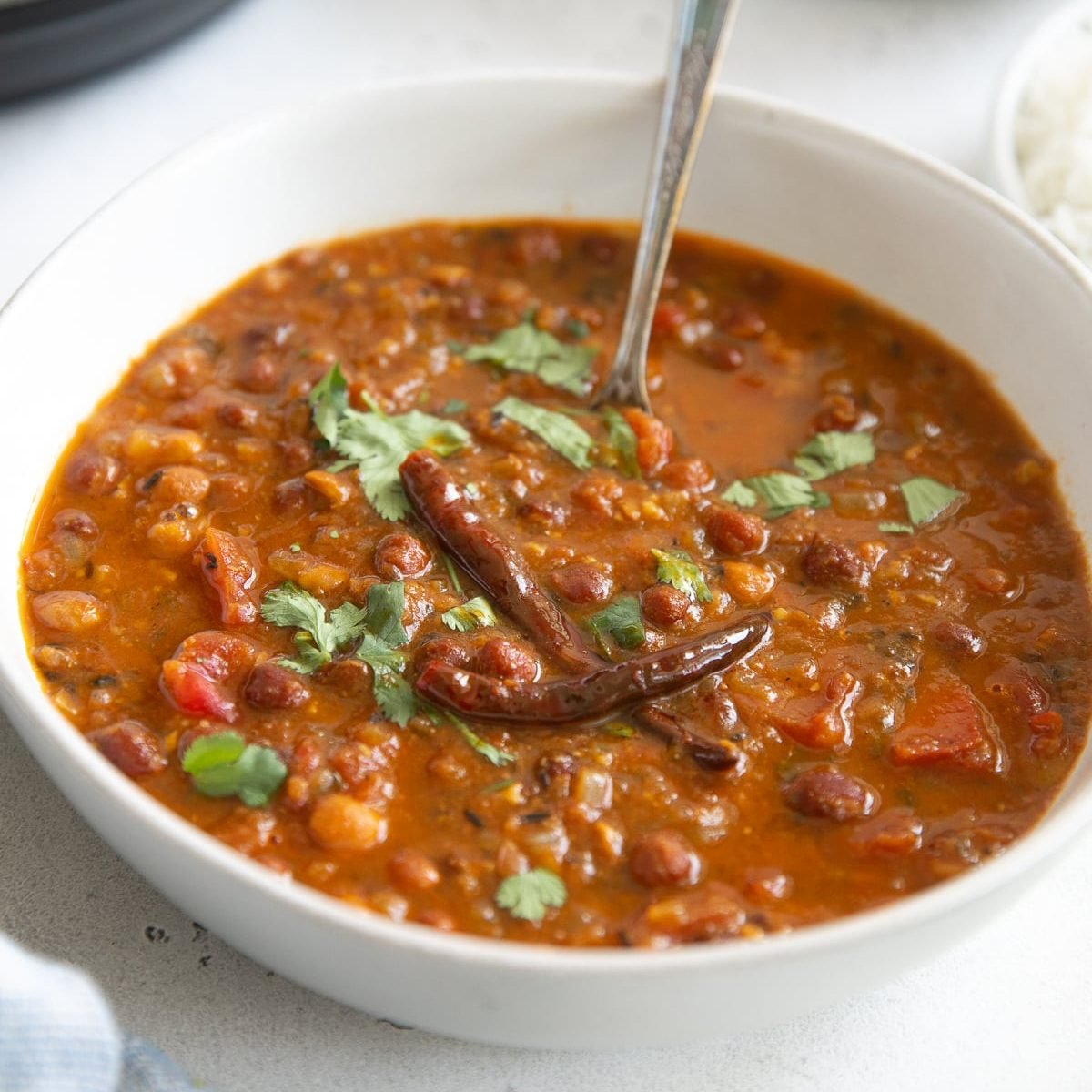 Image of a white bowl filled with fully cooked and prepared chana masala garnished with cilantro.