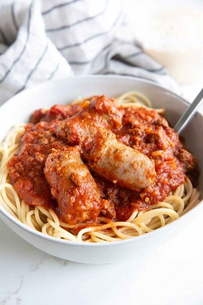 Image of a white bowl filled with spaghetti covered with spaghetti sauce made with ground beef and topped with sausage.