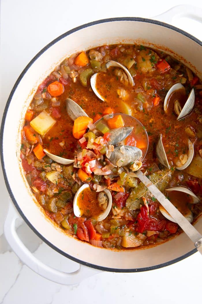 Overhead image of a large pot of Manhattan clam chowder filled with carrots, celery, onion, potatoes, little neck clams, all simmering in a tomato and clam broth.