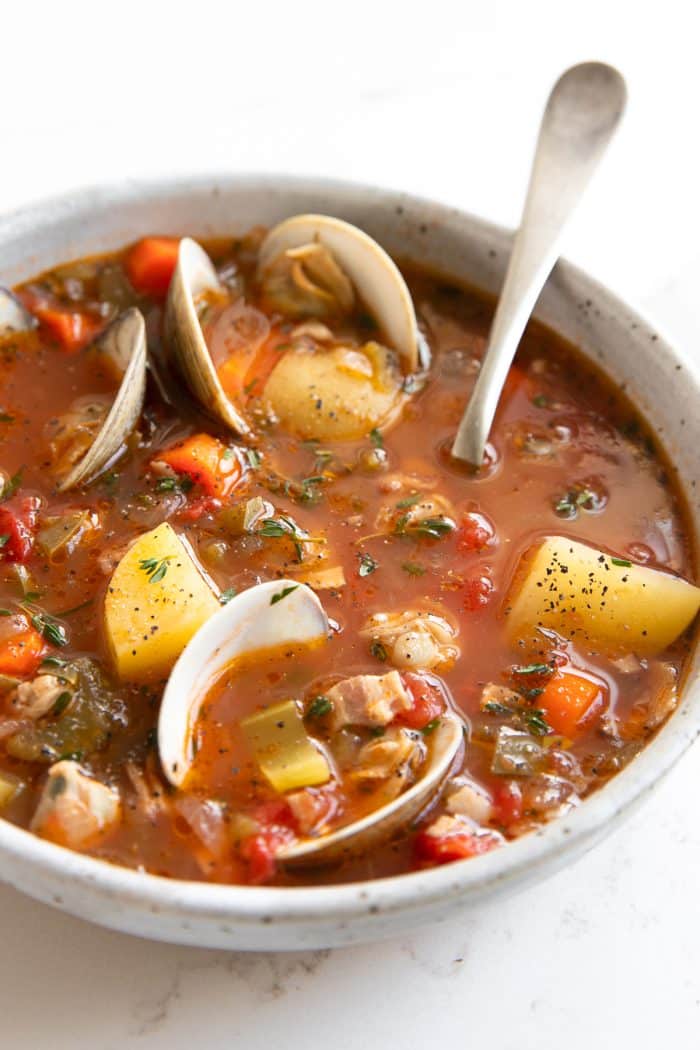 Image of a white soup bowl filled with homemade Manhattan clam chowder recipe made with little neck clams, potatoes, carrots, in a light tomato clam broth.