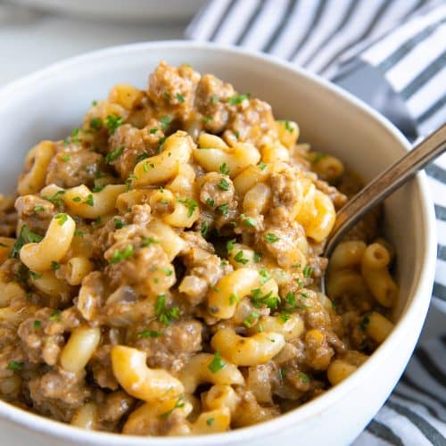 Image of a white bowl filled with homemade one-pot hamburger helper made with ground beef and macaroni noodles garnished with minced parsley.