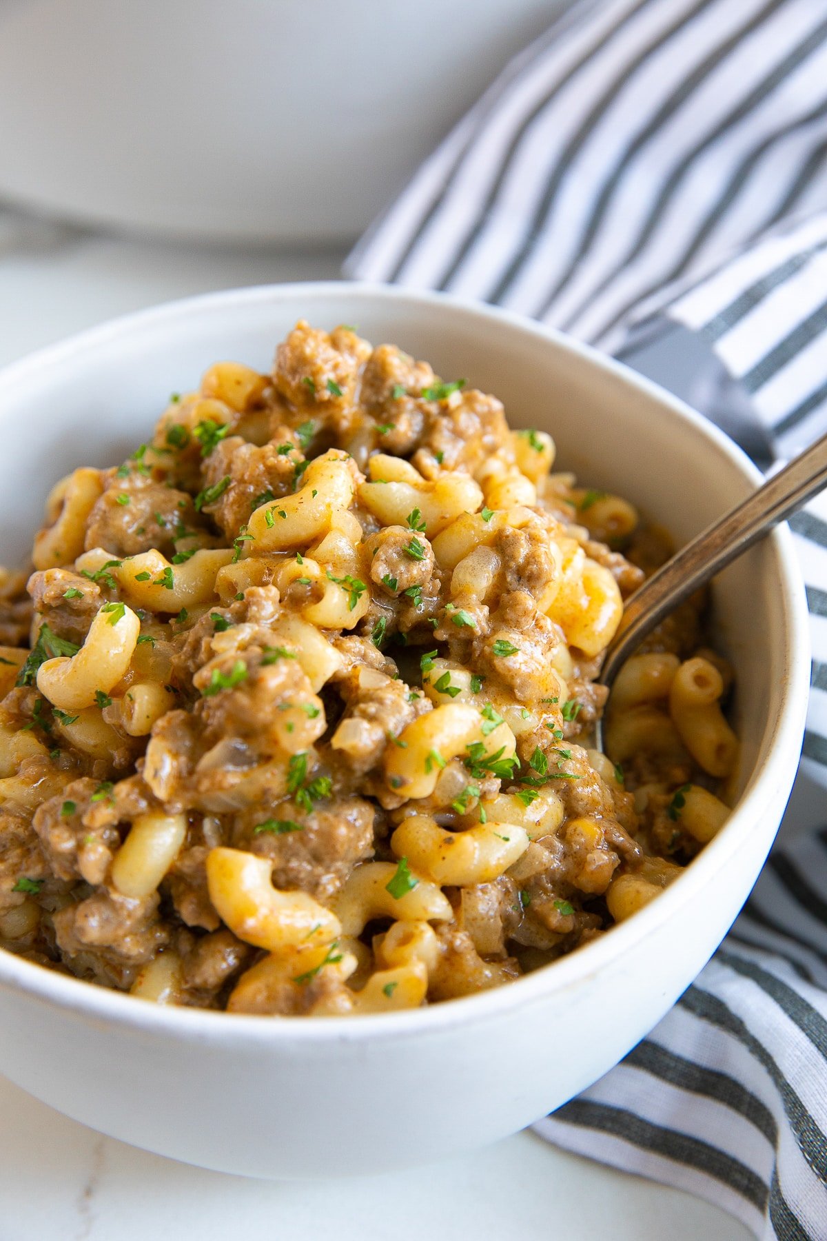 Image of a white bowl filled with homemade one-pot hamburger helper made with ground beef and macaroni noodles garnished with minced parsley.