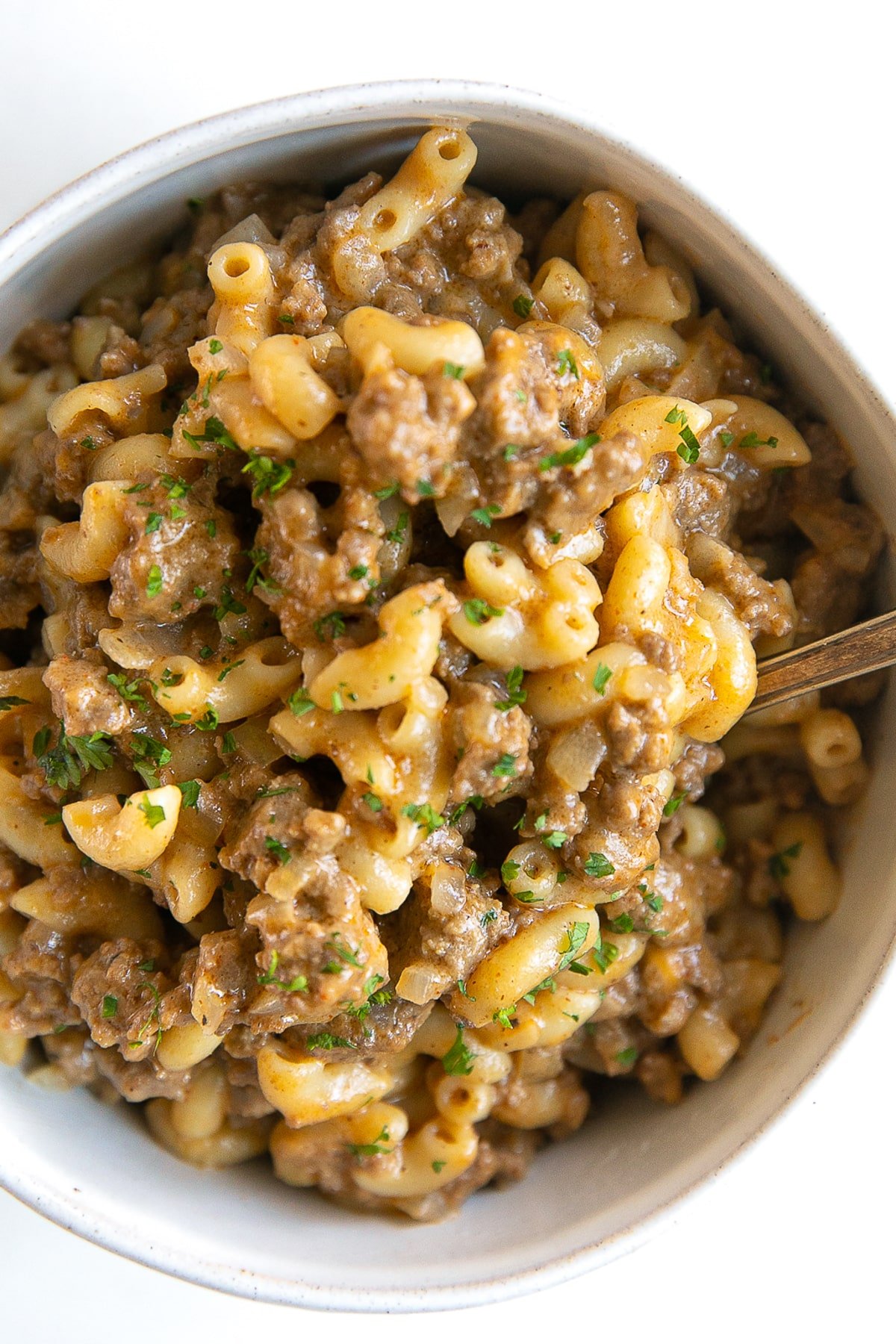 Close up image of a white bowl filled with homemade one-pot hamburger helper and garnished with minced parsley.