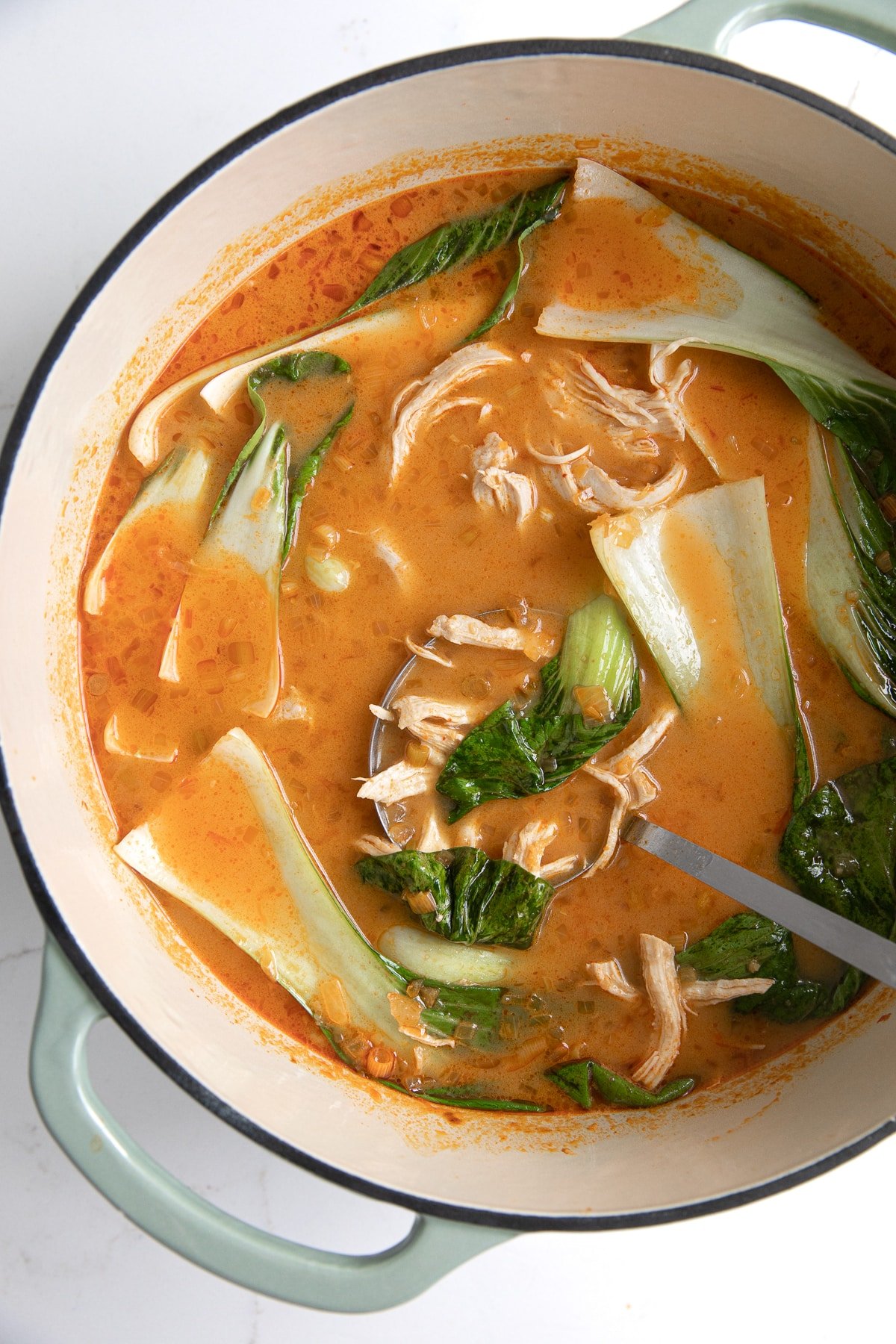 Large pot filled with Thai chicken curry soup with chicken and baby bok choy.