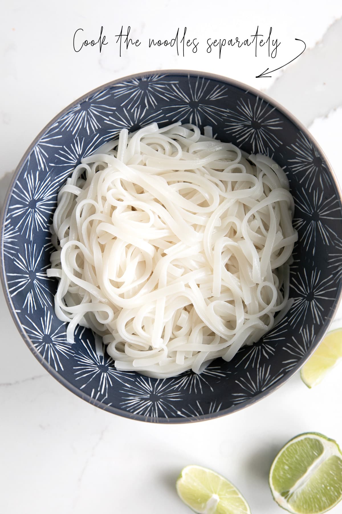 A blue bowl full of cooked rice noodles, with text overlay stating, "cook the noodles separately" with an arrow pointing to noodles.