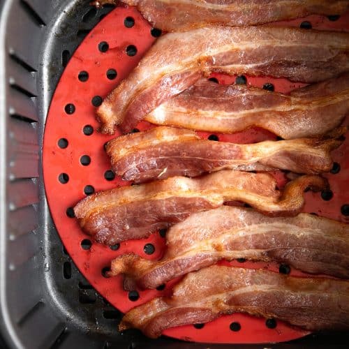 Strips of cooked bacon in a single later inside the basket of an air fryer.