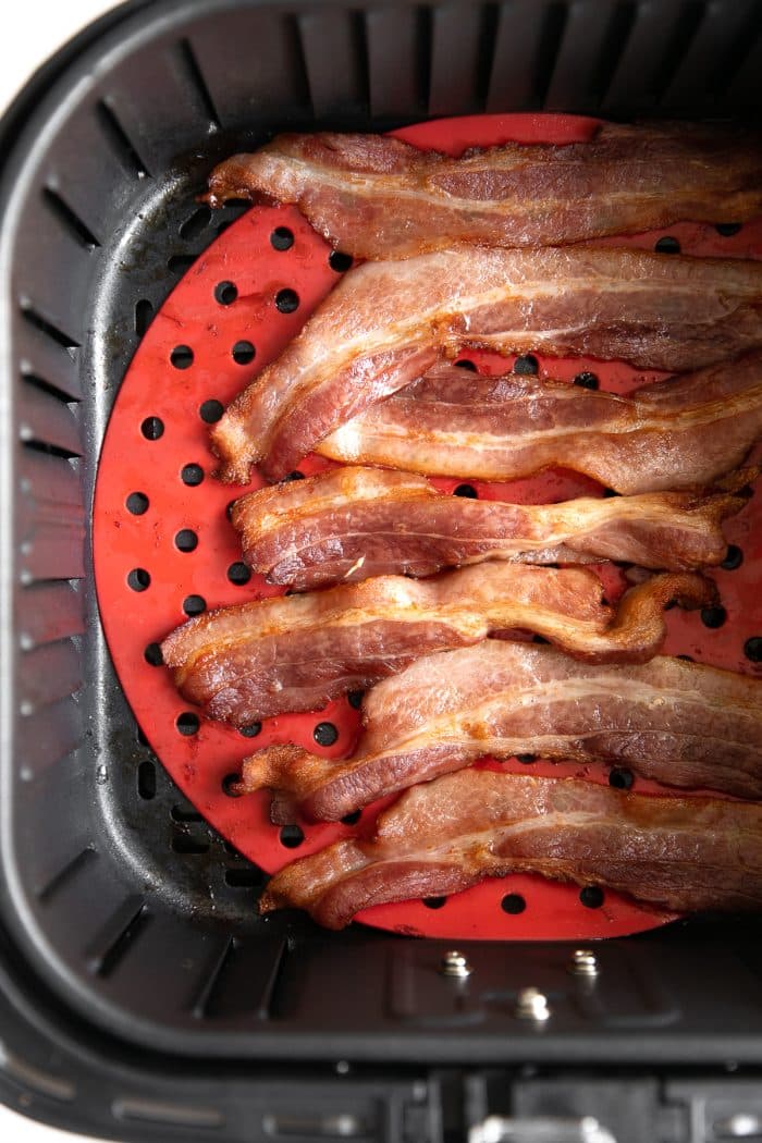 Strips of cooked bacon in a single later inside the basket of an air fryer.