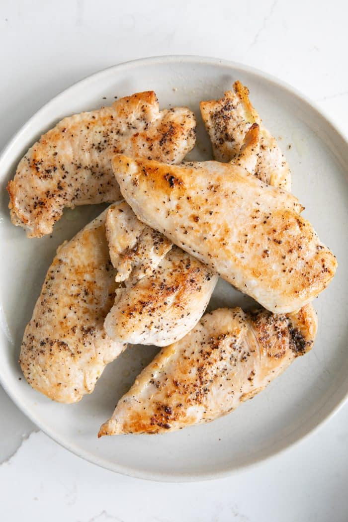 Large white plate filed with seared chicken cutlets seasoned with salt and pepper.
