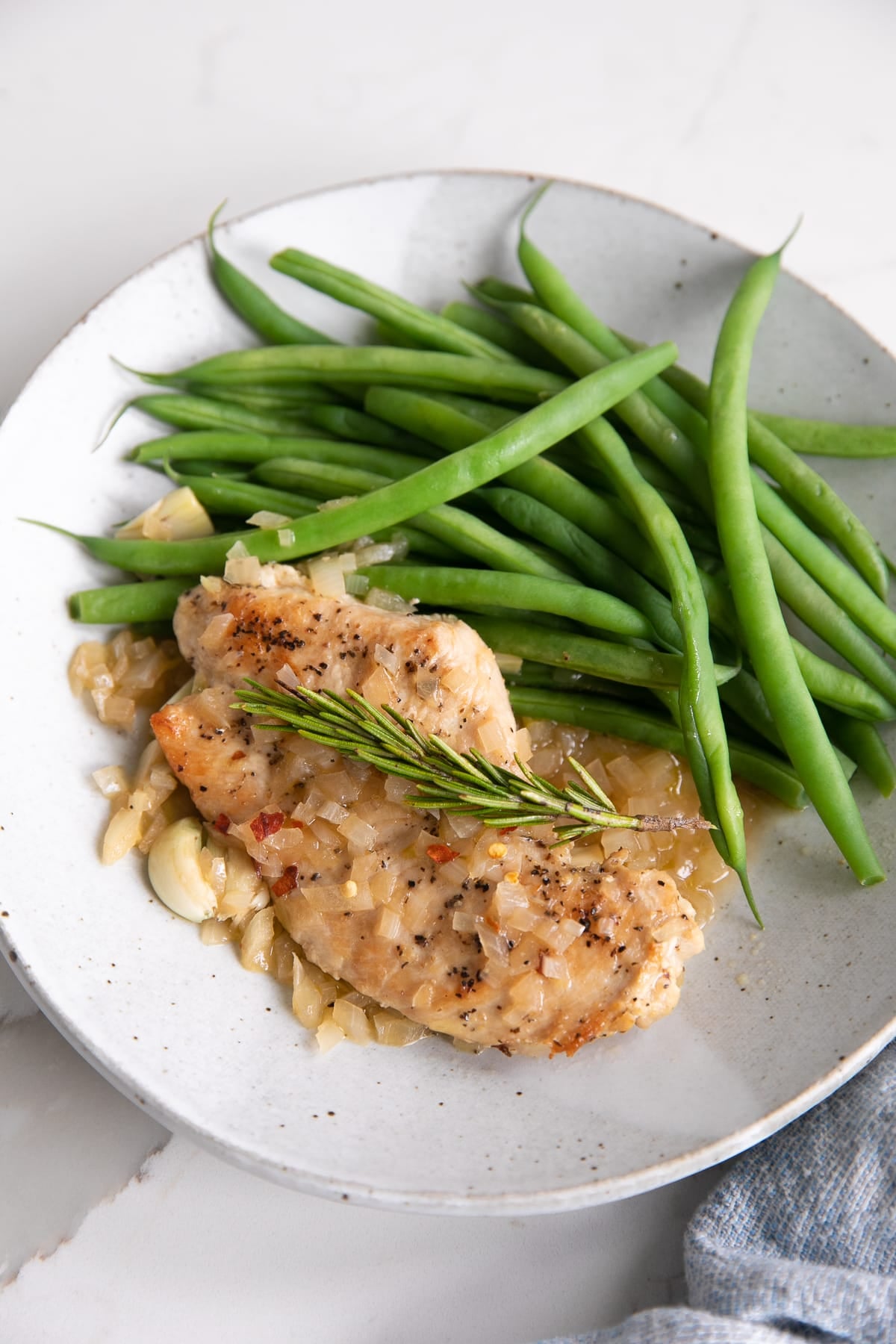 Small dinner plate with one thinly sliced chicken breast and side of green beans covered in a garlic, rosemary, and sherry sauce.