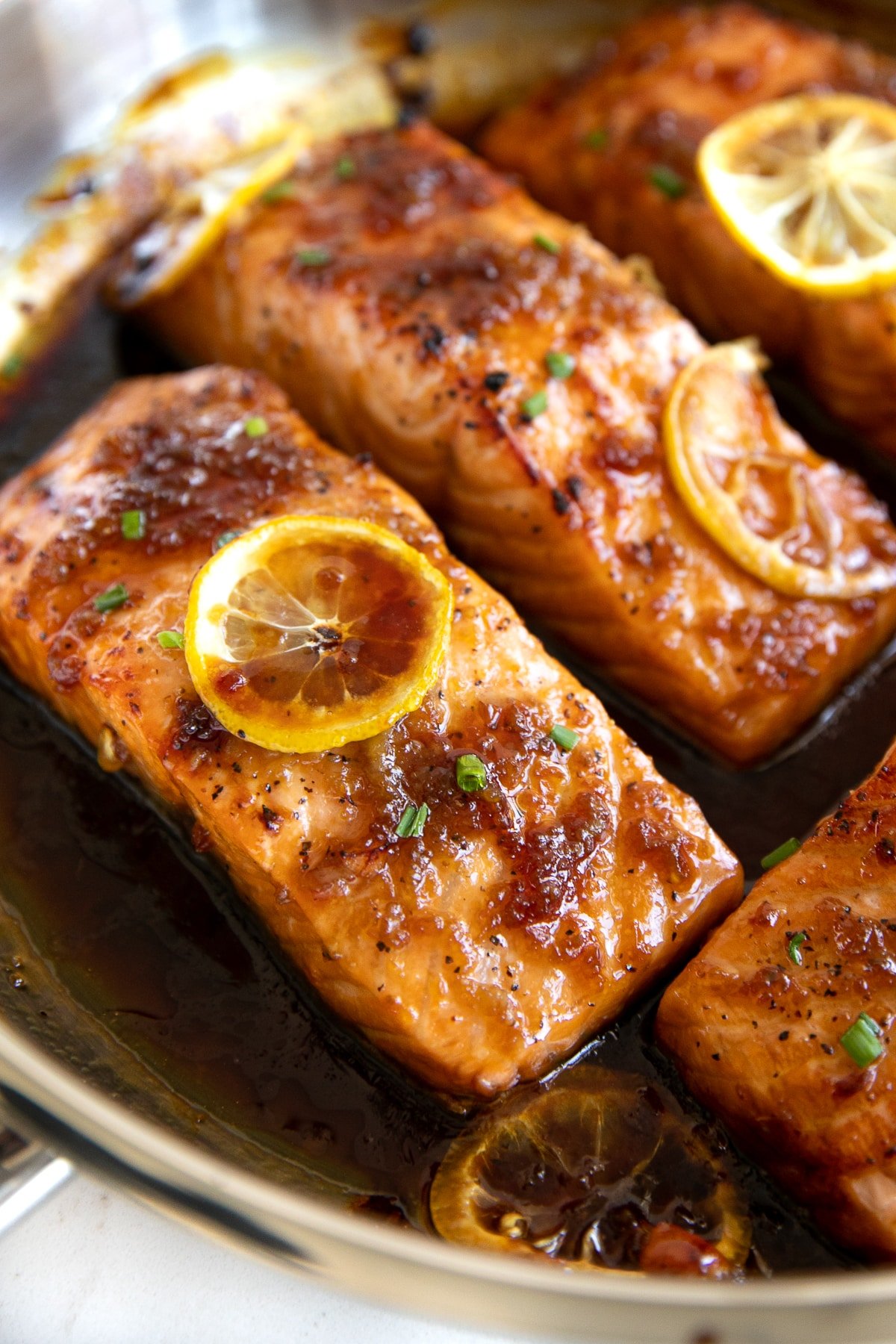 Close up image of honey garlic salmon fillets in a large stainless steel pan.