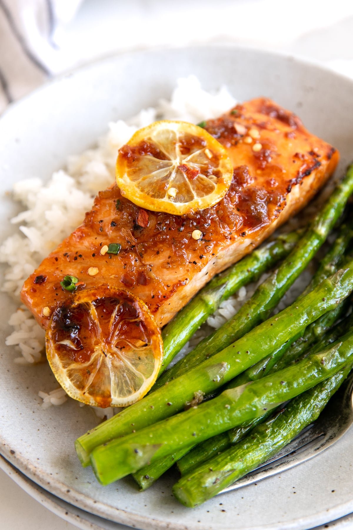 Medium sized dinner plate filed with white rice, cooked asparagus, and one salmon fillet covered in a honey garlic sauce.