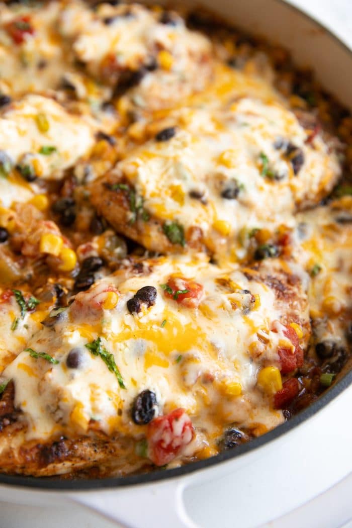 Large skillet filled with thinly sliced chicken breasts cooked and covered with a mixture of onions, black beans, tomatoes, and sweet corn and smothered in melted cheese.