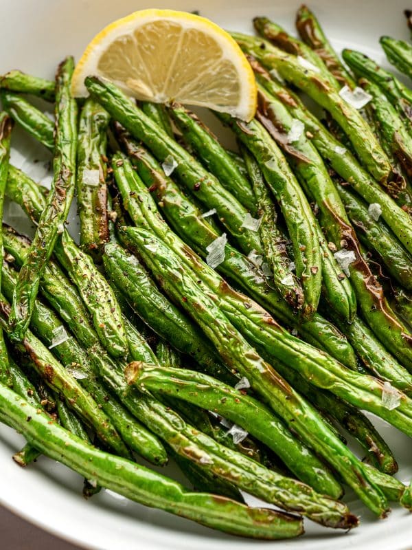 Close-up of air fryer green beans garnished with lemon wedge and sea salt.
