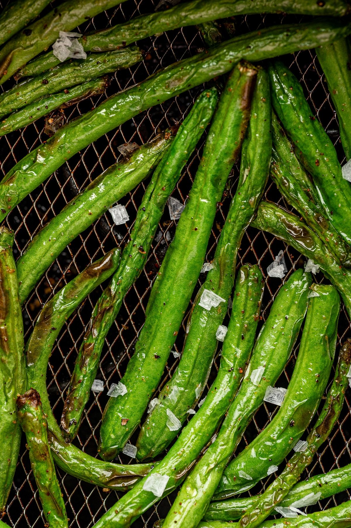 Air-fried green beans sprinkled with flaky sea salt in an air fryer basket.
