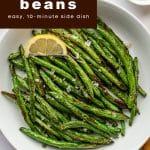 Overhead photo of air fryer green beans in a white bowl topped with lemon wedge and flaky salt.
