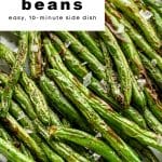 Close-up of crispy air fryer green beans with sea salt and lemon slice in a white bowl.