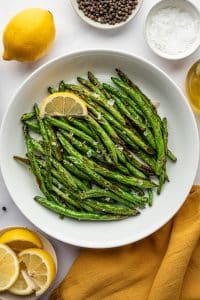 Cooked air fryer green beans served in a white bowl with lemon wedge and flaky salt.