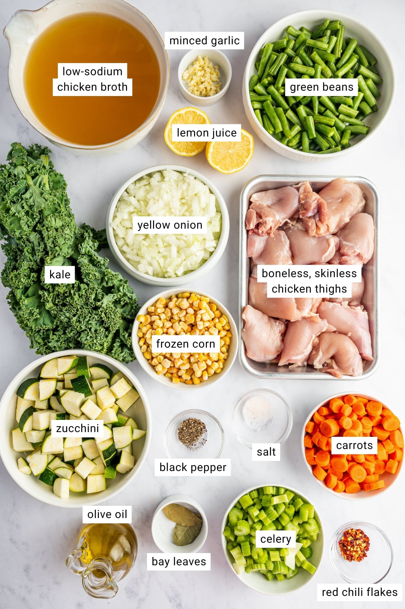 Labeled ingredients for chicken vegetable soup including low-sodium chicken broth, boneless skinless chicken thighs, yellow onion, carrots, celery, green beans, zucchini, kale, frozen corn, minced garlic, lemon juice, olive oil, bay leaves, salt, black pepper, and red chili flakes.