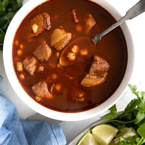 Overhead image of a white bowl filled with authentic pozole surrounding by plates filled with optional garnishes.