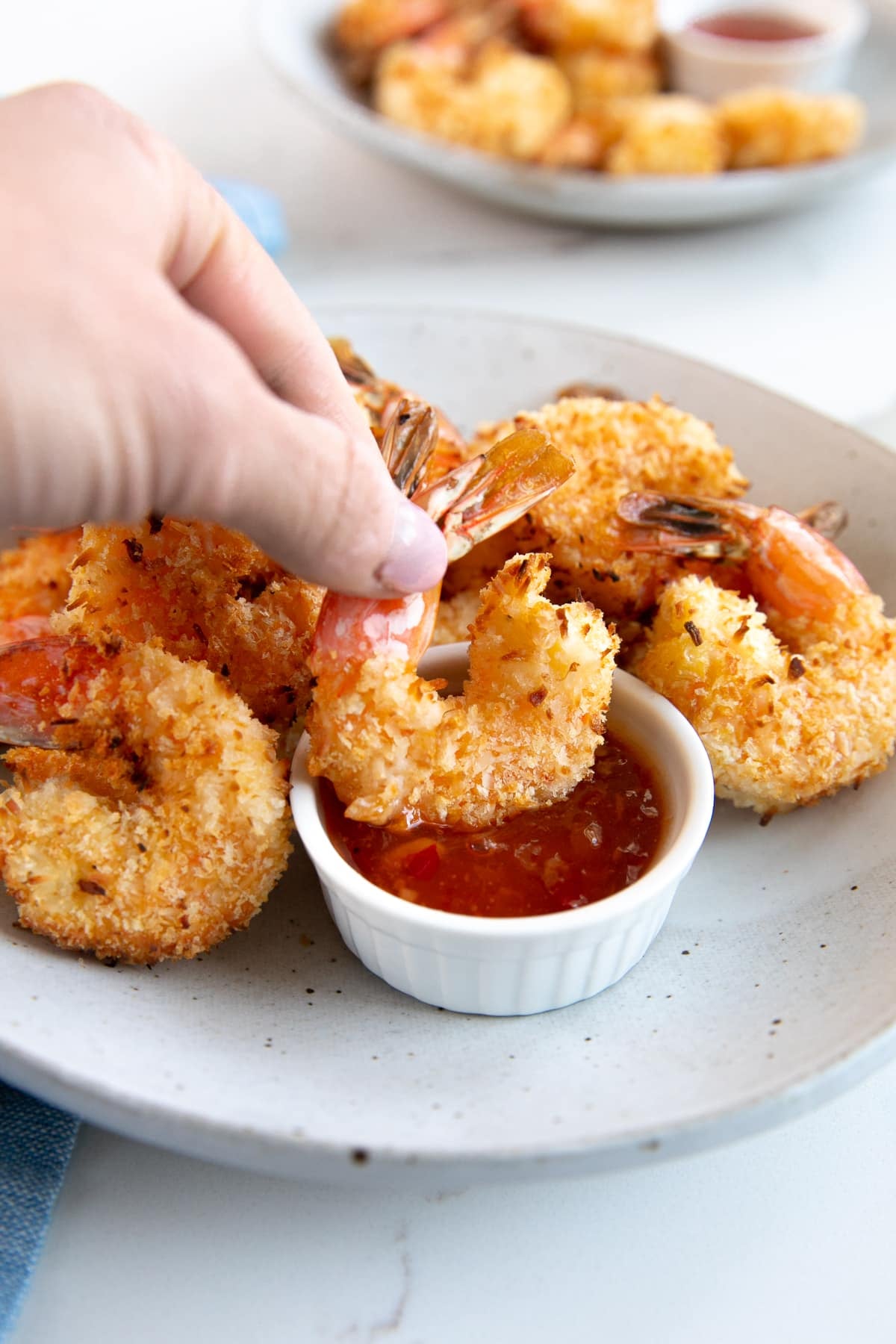 Hand holding one coconut shrimp by the tail and dipping it into homemade apricot dipping sauce.