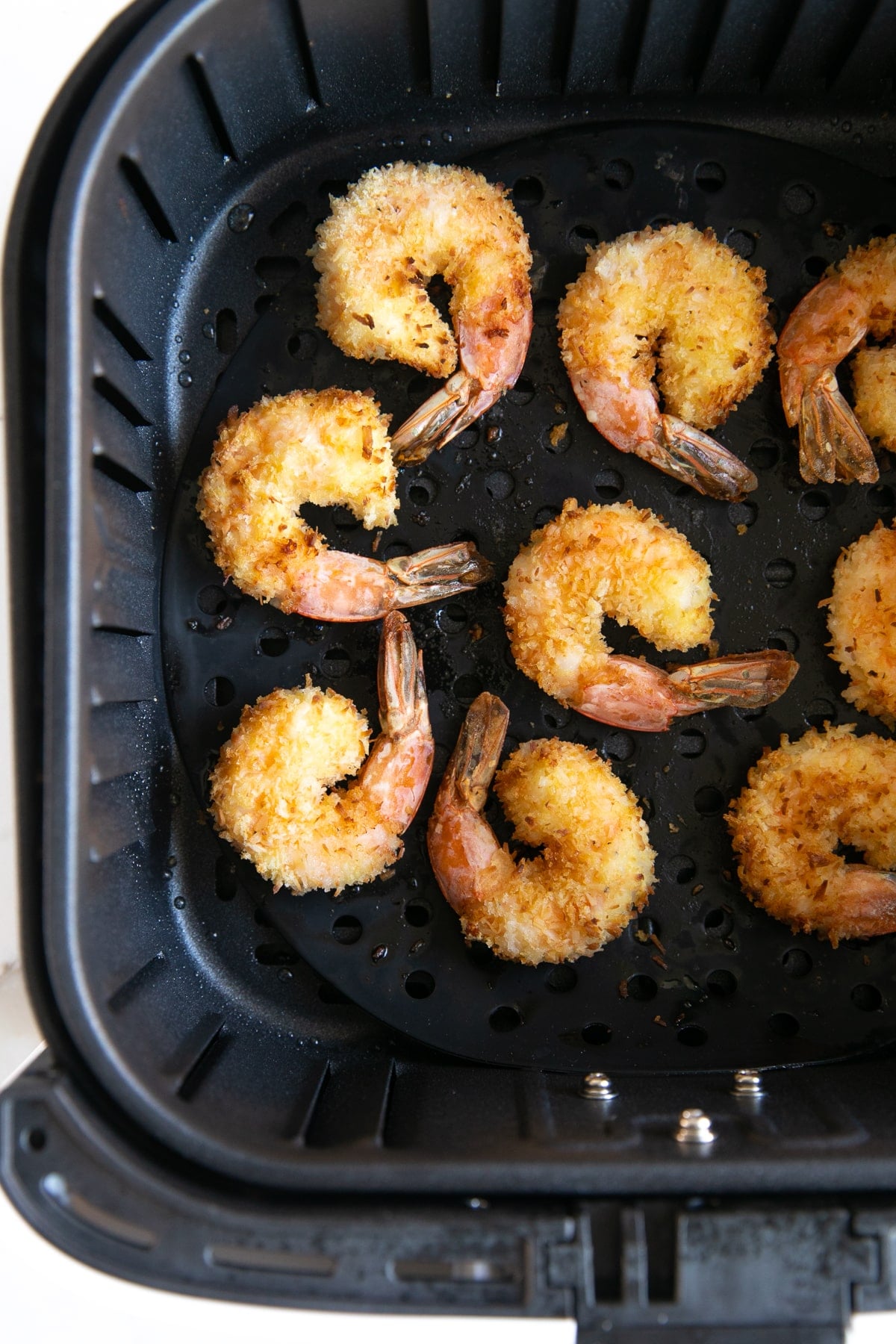 Cooked coconut shrimp in the basket of a large air fryer.