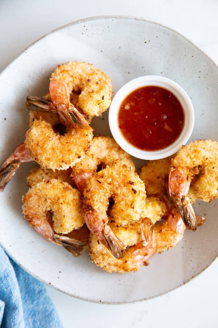 Overhead image of a serving plate filled with air fryer coconut shrimp and a small bowl of apricot dipping sauce.