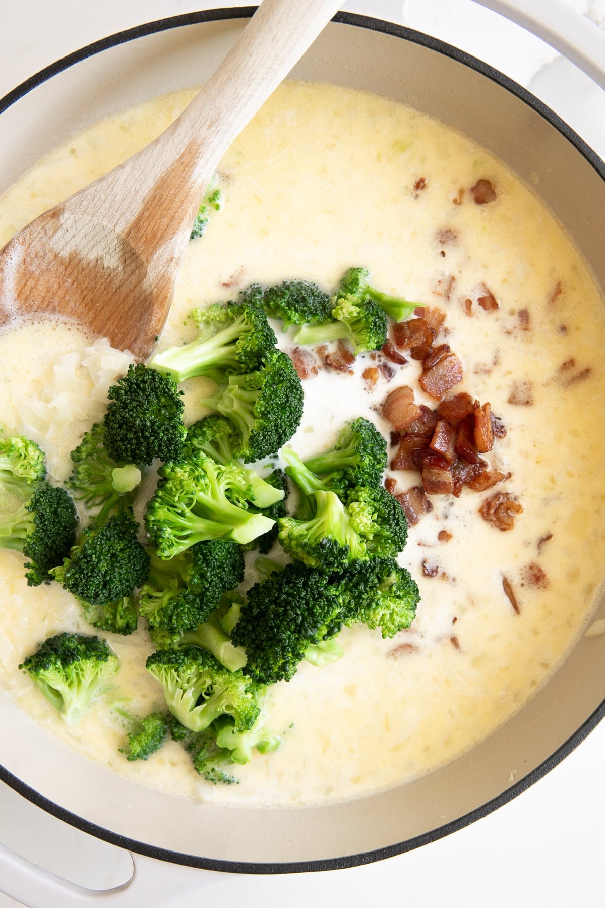 Image of a large white ceramic skillet filled with homemade cream sauce and filled with blanched broccoli florets and cooked bacon bits.