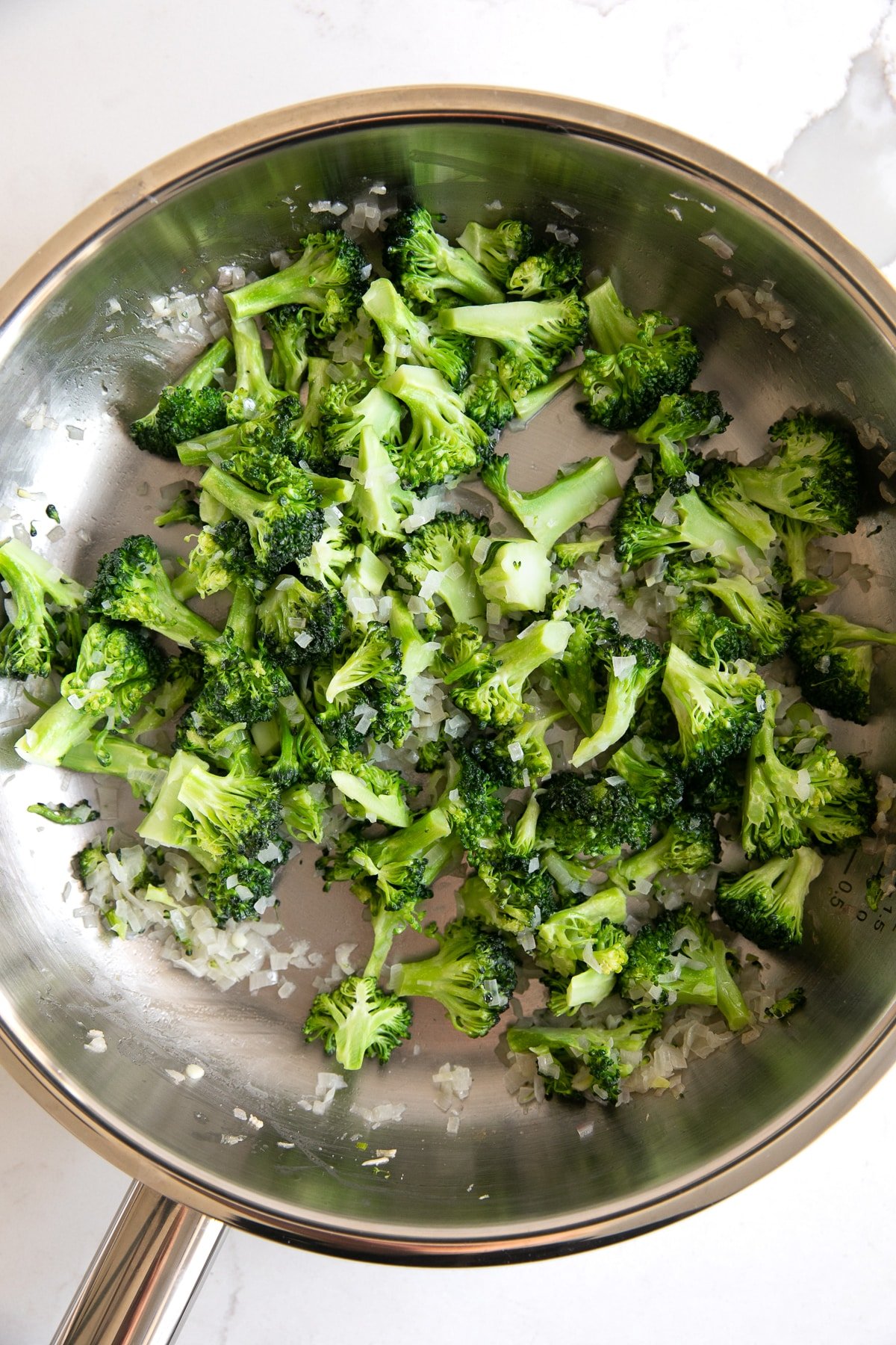 Image of a stainless steel skillet filled with sauteed shallots, garlic, and broccoli florets.