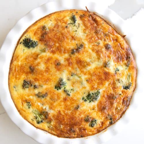 Image of a cooked crustless quiche filled with broccoli in a white pie dish.