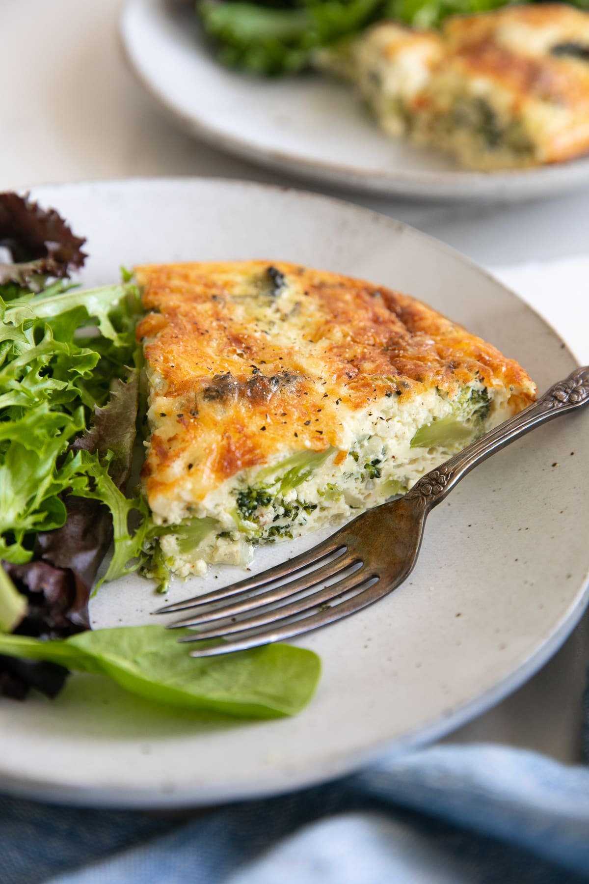 Small serving plate served with a single slice of crustless quiche and a side of mixed green lettuce.