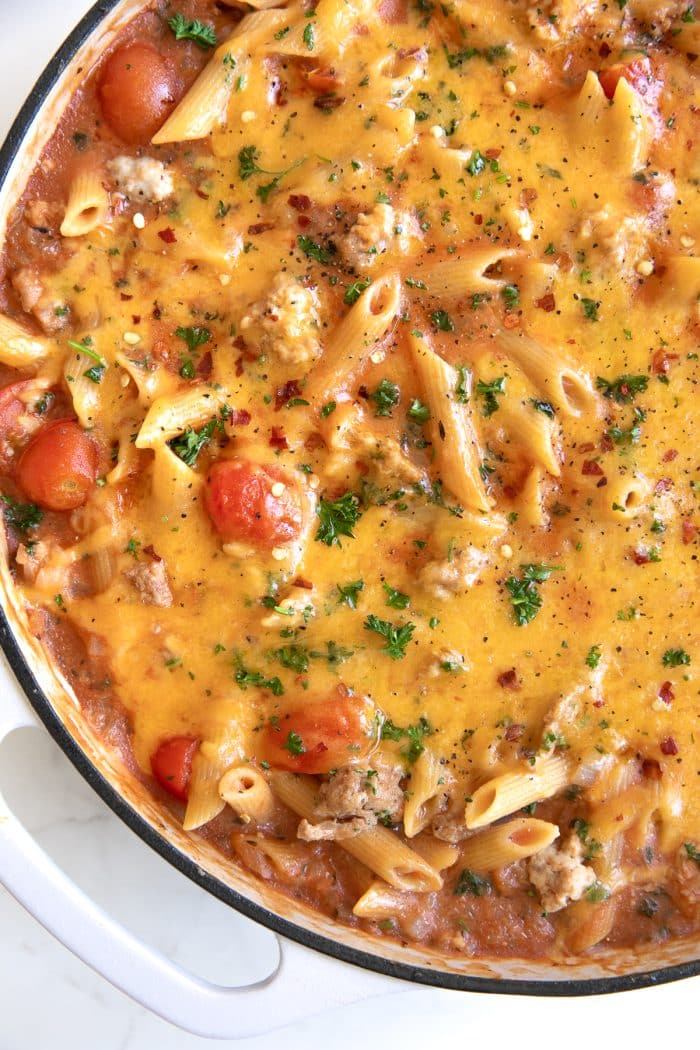 Large white skillet filled with ground turkey and penne pasta mixed in a creamy tomato sauce and topped with gooey melted cheddar cheese.