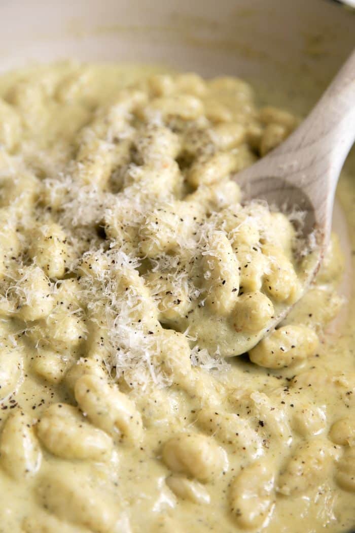 Image of a white ceramic pan filled with cooked gnocchi in a pesto creamy sauce and covered with freshly grated parmesan cheese.