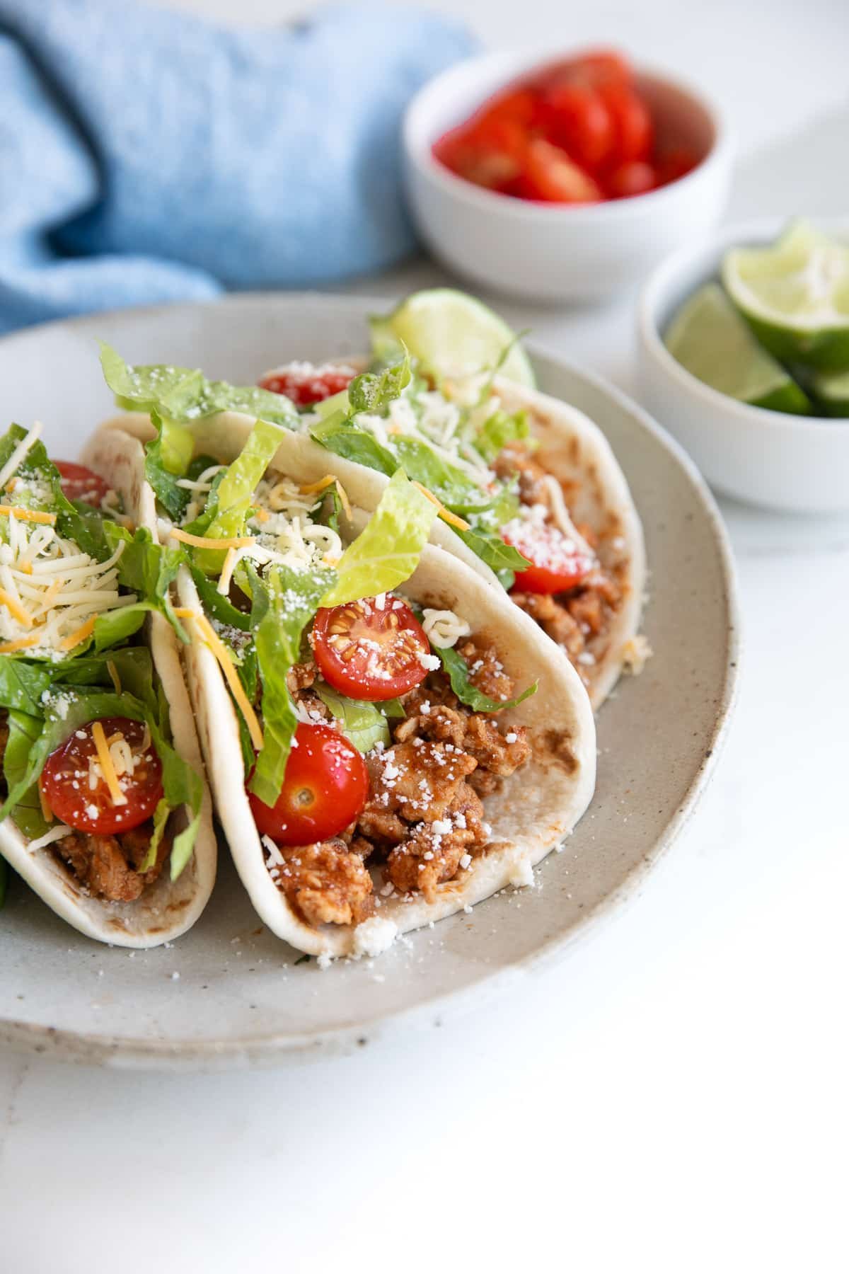 Three ground turkey tacos filled with ground turkey taco meat and topped with tomatoes, lettuce, and cheese, on a small serving plate.