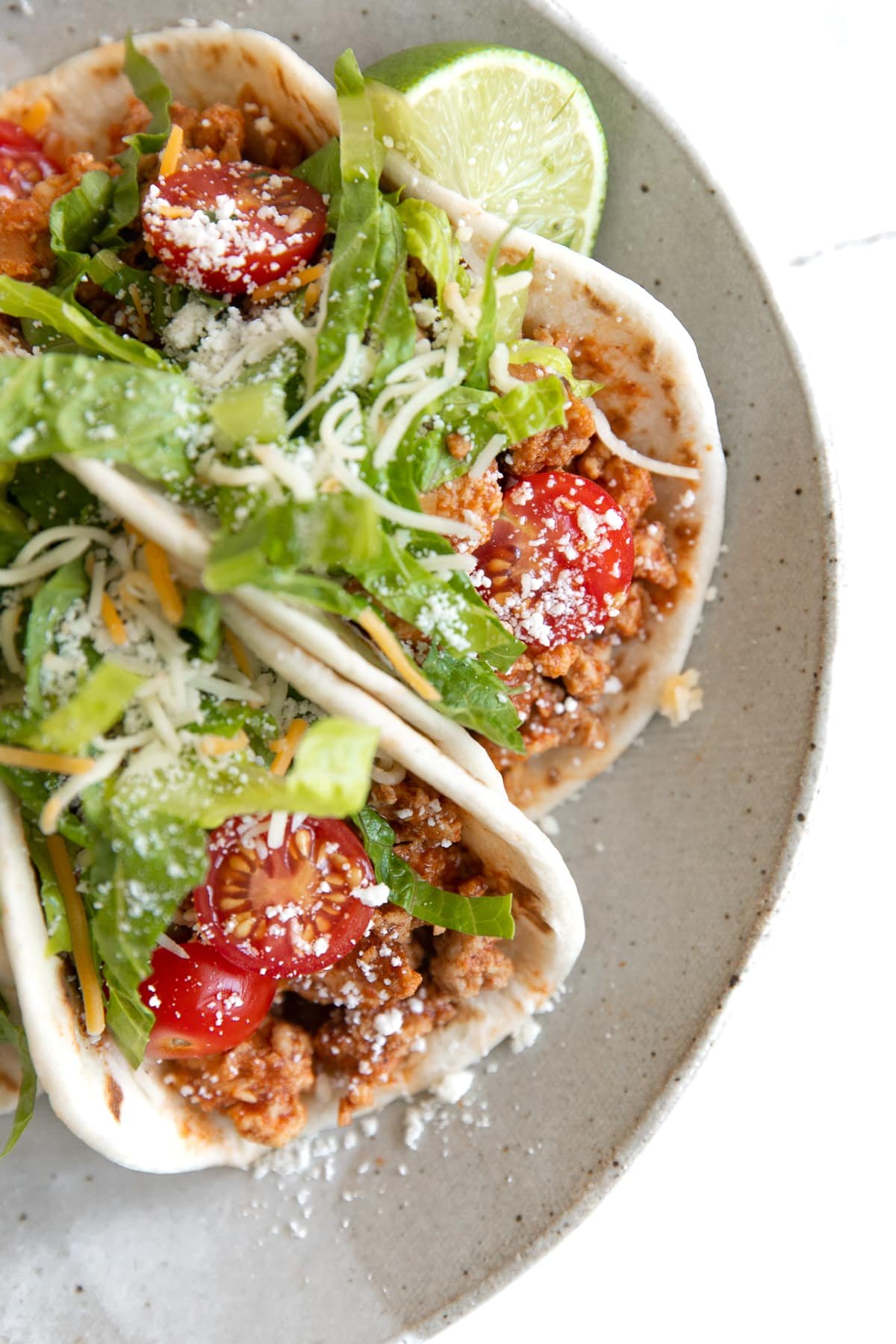 Overhead image of two soft tacos filled with ground turkey taco meat and topped with halved cherry tomatoes, chopped lettuce, and cheese.