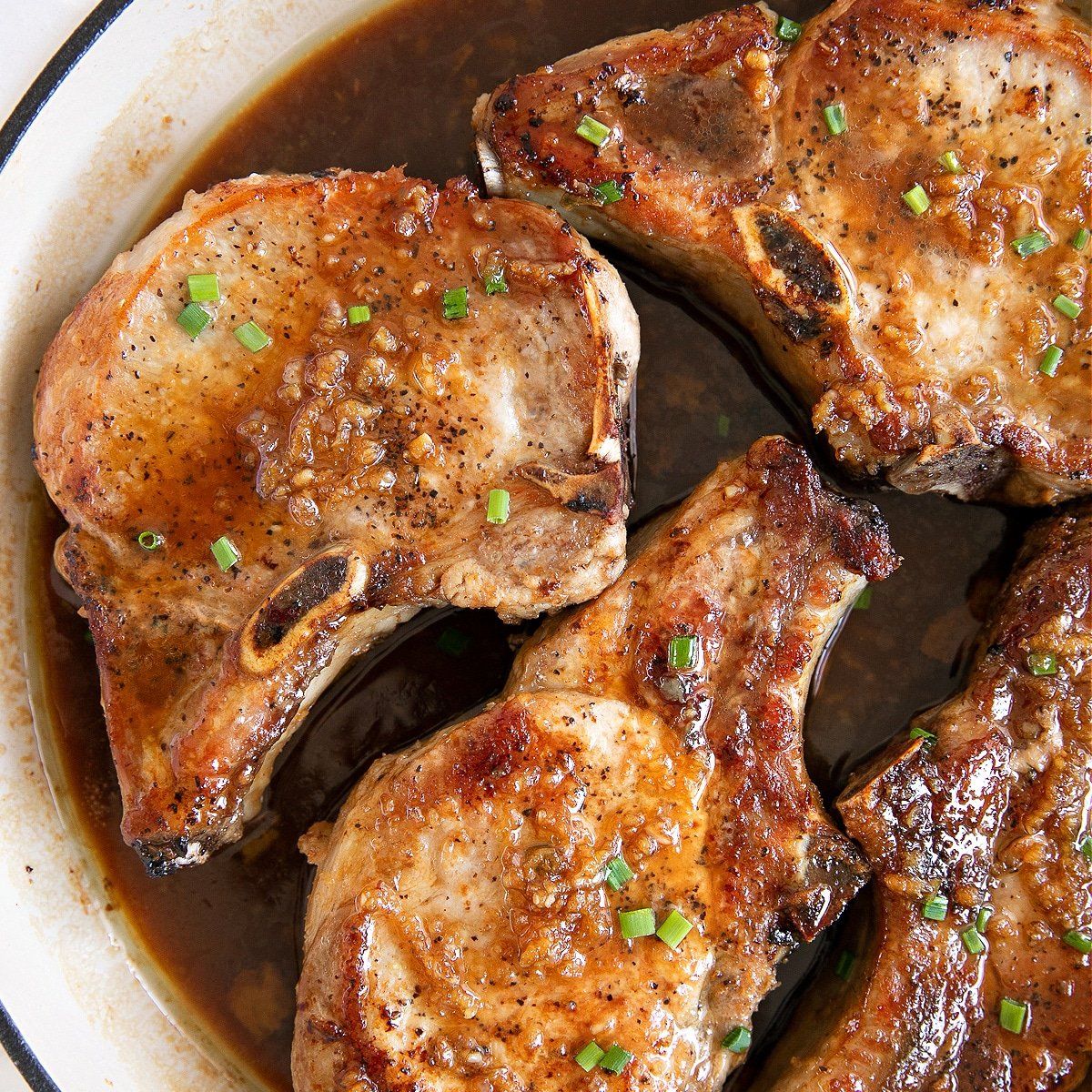 Four seared bone-in pork chops resting in a homemade honey garlic sauce in a large skillet.