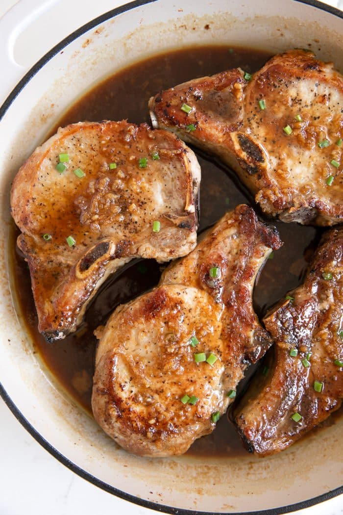 White skillet filled with seared bone-in pork chops simmered in a sweet and sticky honey garlic sauce.